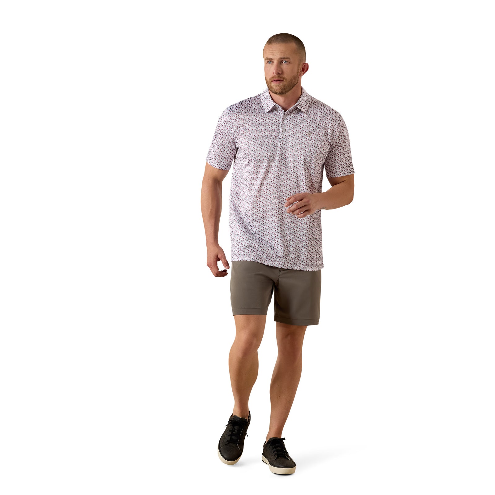 A man modeling a short-sleeve collared polo shirt with a small geometric pattern in pink and white, paired with olive brown shorts and black sneakers, against a solid white background.