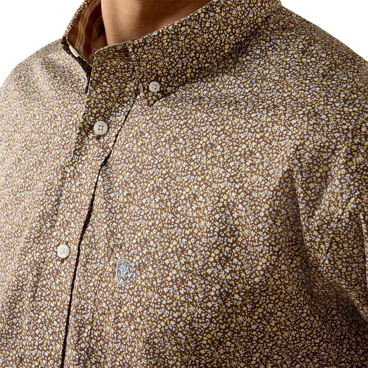 Close-up of a men's button-down shirt featuring a dense, small-scale floral or ditsy print in brown, beige, and white, worn by a model.