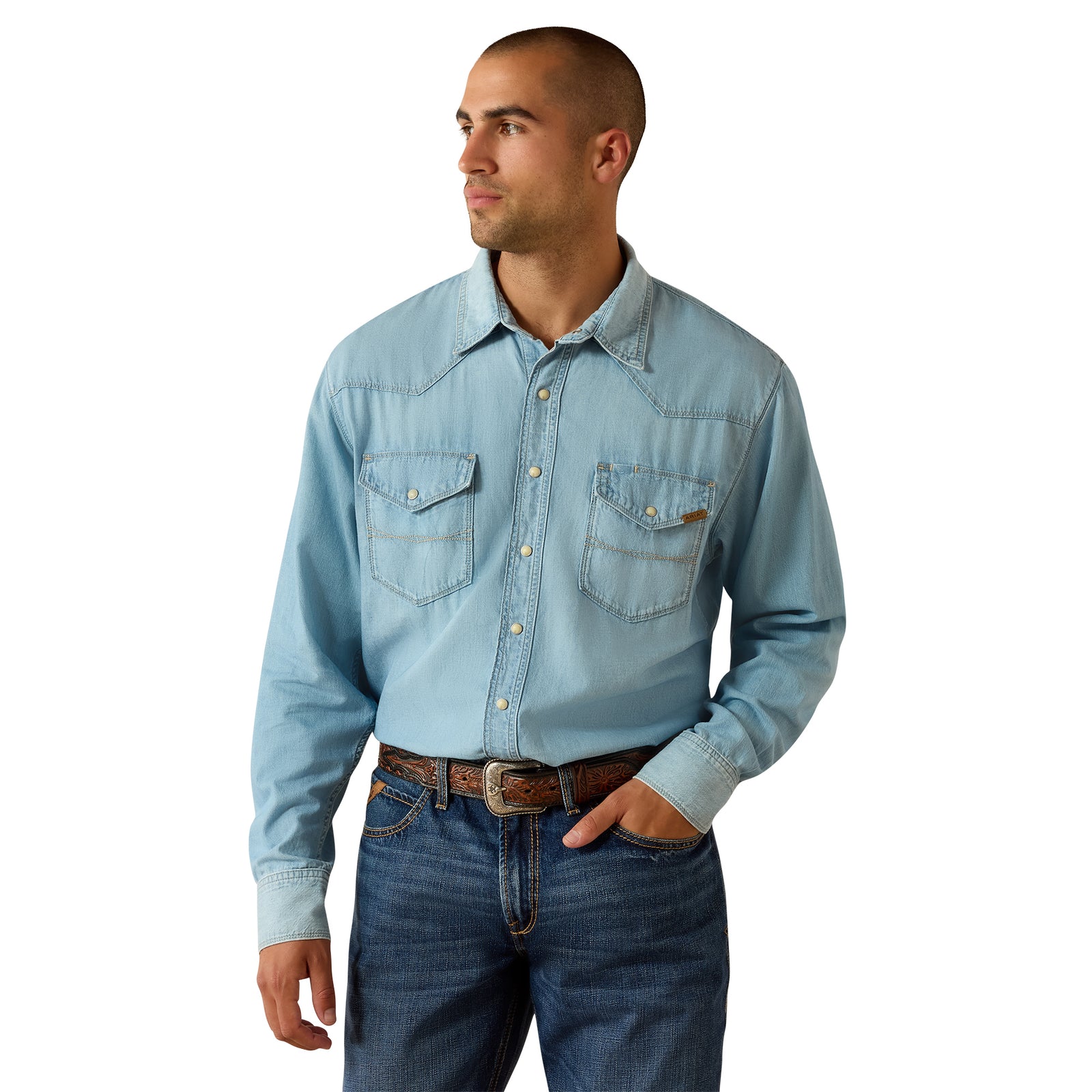 A man wearing a light blue denim western long-sleeve shirt with two chest pockets and blue jeans, standing against a plain white background.
