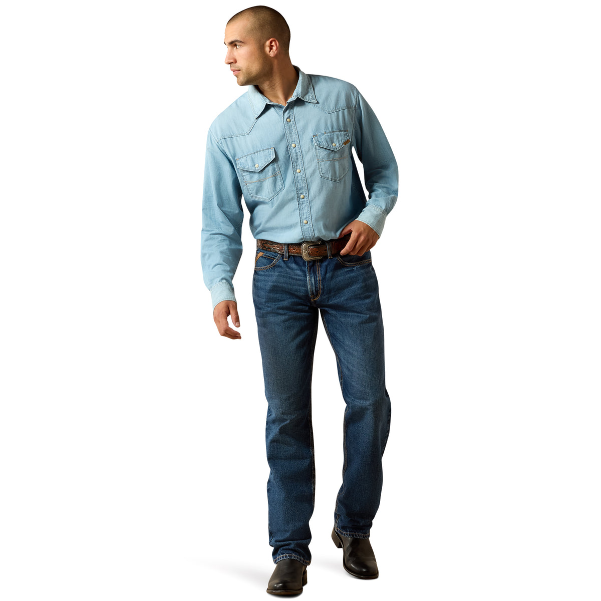 A man wearing a light blue western-style long-sleeve button-up shirt, dark blue jeans, a brown belt, and black shoes, standing against a plain white background.
