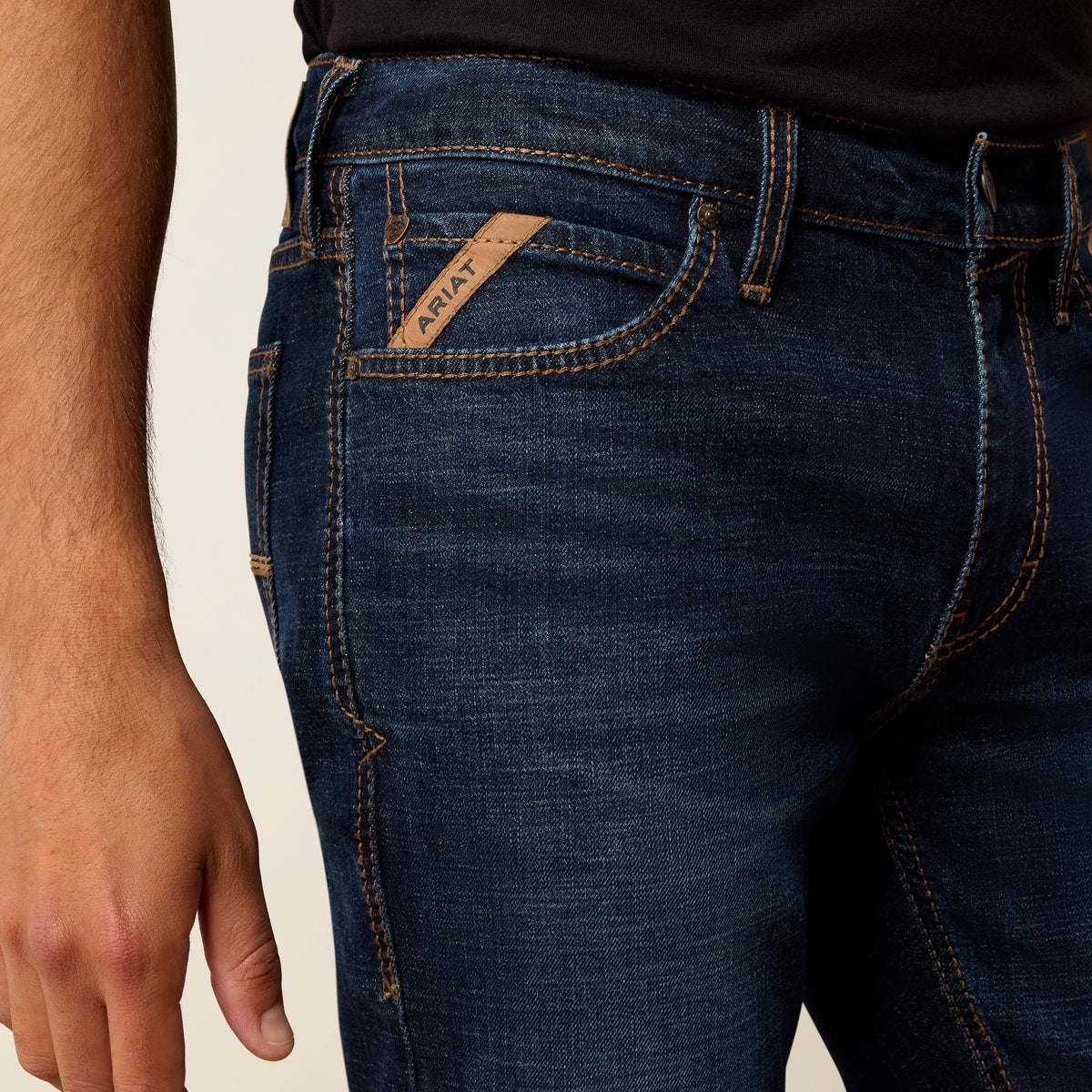 Close-up of dark blue jeans with a brand label on a beige background