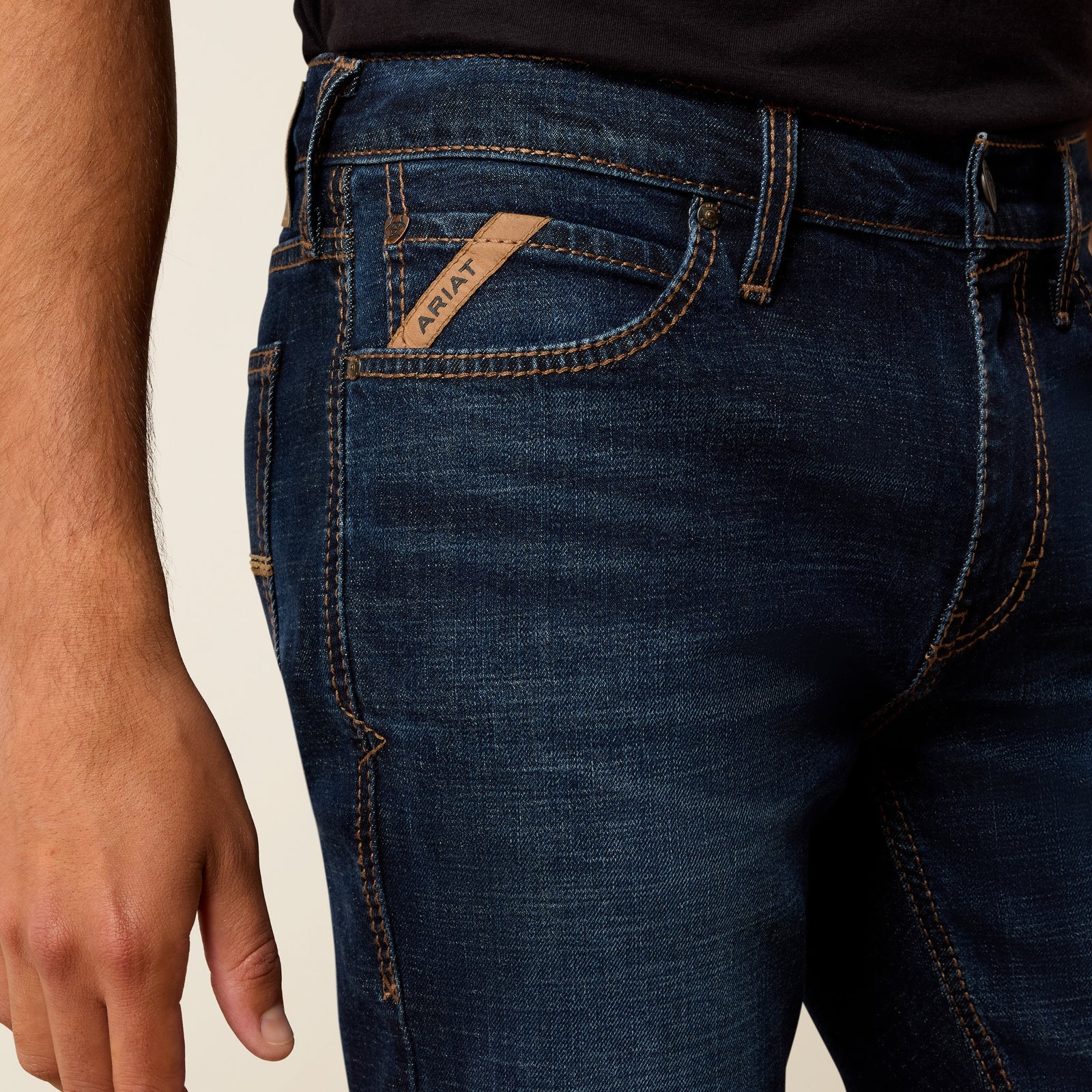Close-up of dark blue jeans with a brand label on a beige background