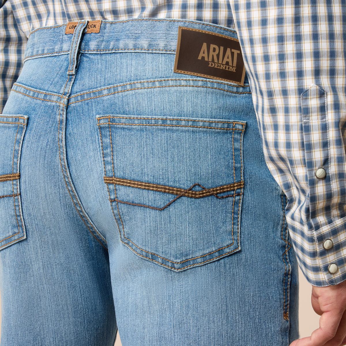 Close-up of blue jeans with Ariat logo, worn with a plaid shirt.