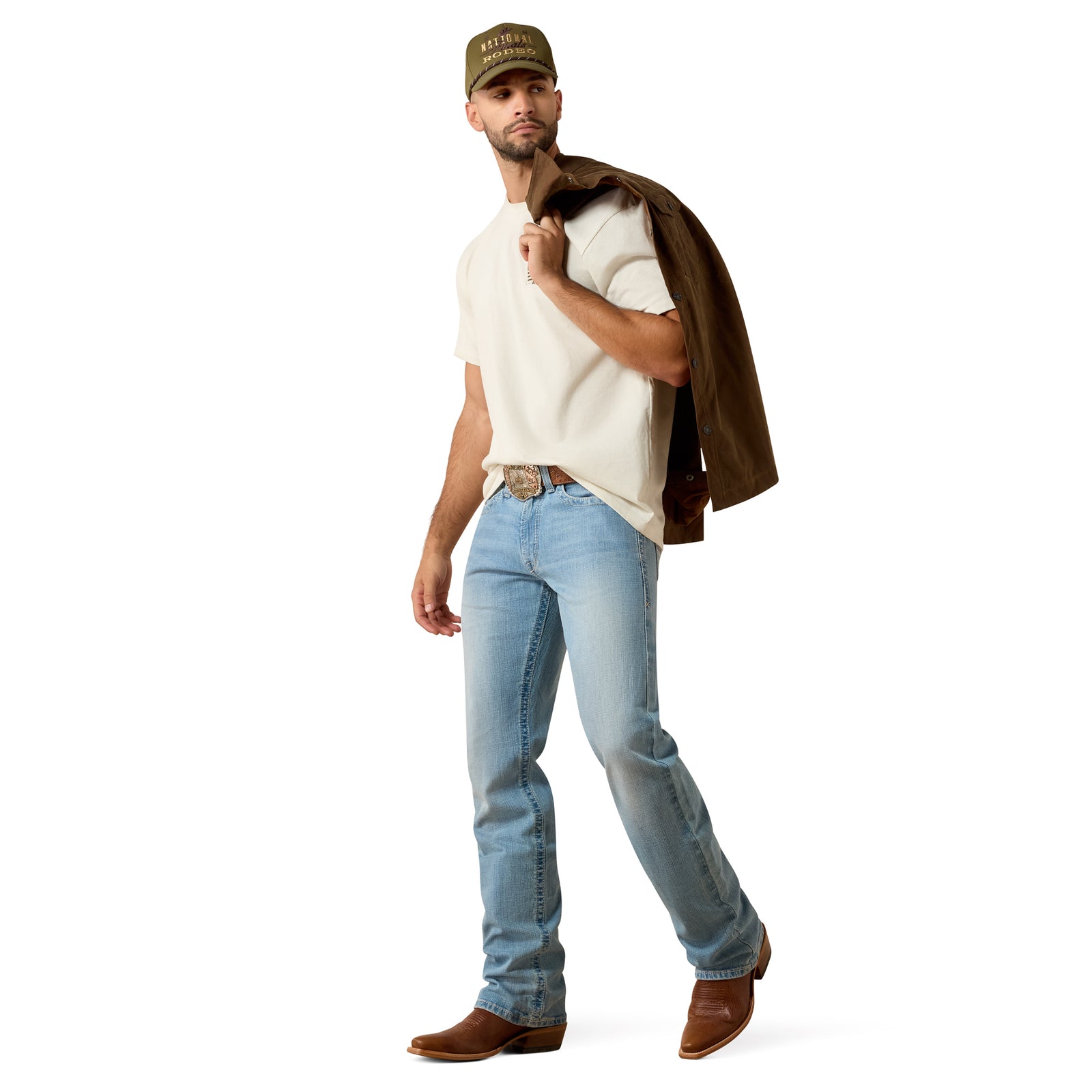 Man wearing a white shirt, blue jeans, brown boots, and a cap, holding a brown jacket.