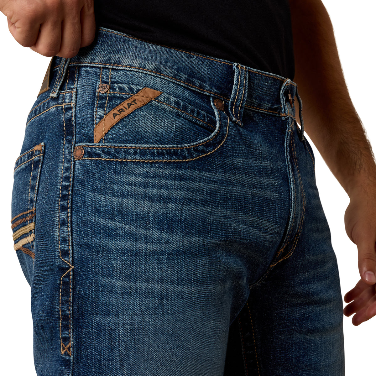 Close-up of blue jeans with ARIAT branding on a white background