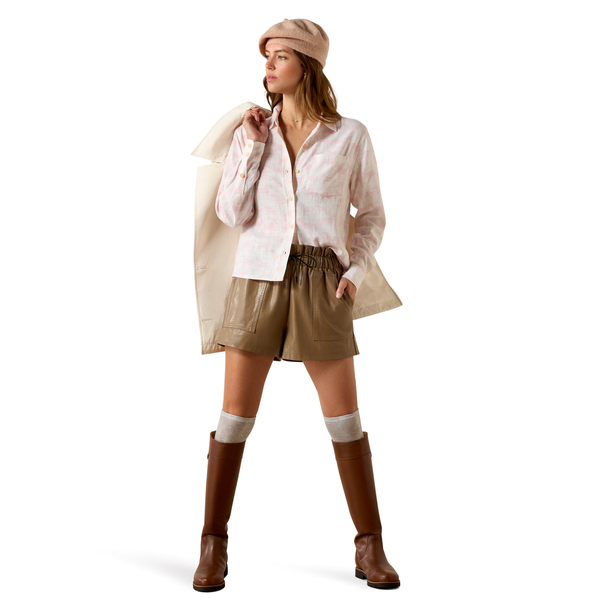 Woman wearing a white shirt, beige shorts, brown boots, and a beige hat on a white background
