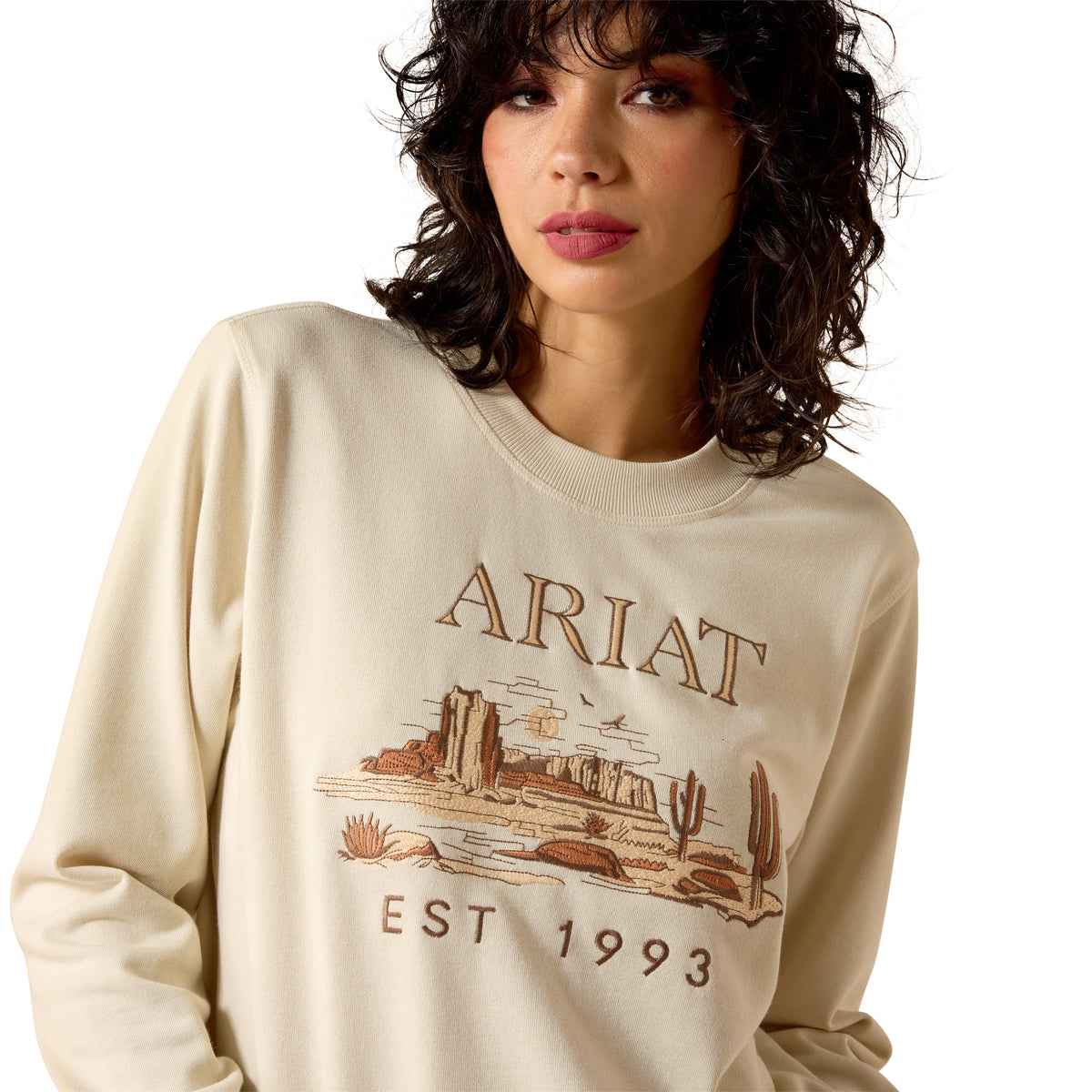 Woman wearing a beige Ariat sweatshirt with a graphic design on a white background