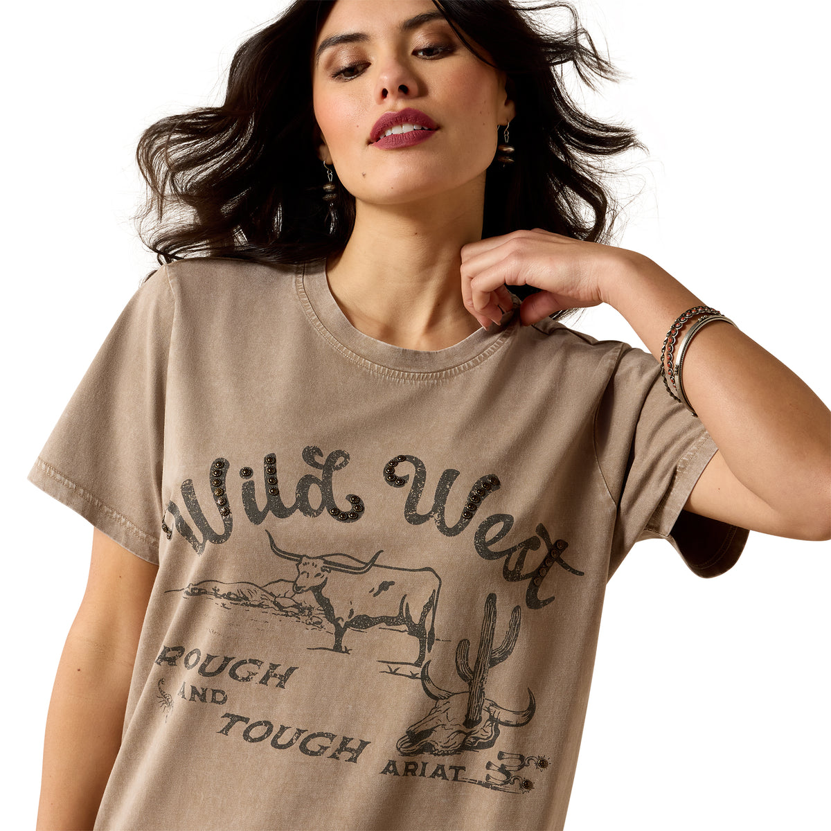 A woman wearing a beige graphic t-shirt with a distressed 'Wild West Tough and Touched' print featuring a steer and cactus design, set against a plain white background.
