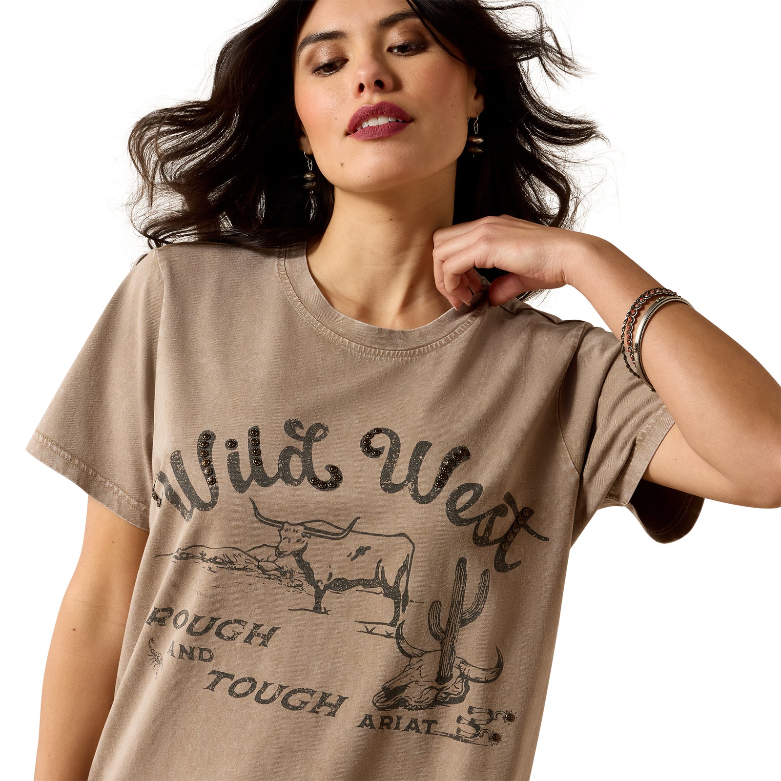 A woman wearing a beige graphic t-shirt with a distressed 'Wild West Tough and Touched' print featuring a steer and cactus design, set against a plain white background.