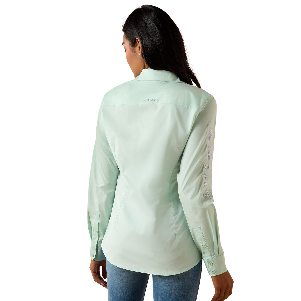 A woman shown from the back wearing a light mint green long-sleeve button-up shirt with embroidered details on the sleeve, paired with blue jeans, against a plain white background.