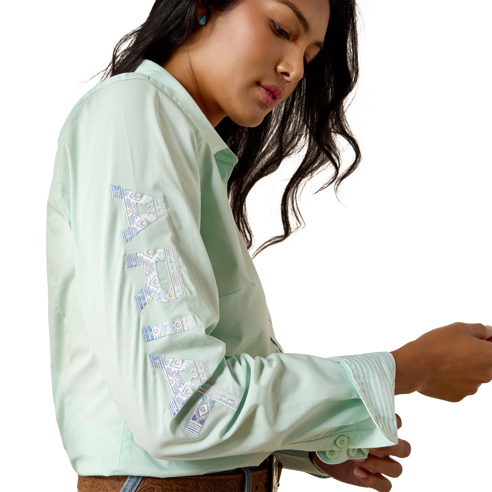 A woman wearing a mint green long-sleeve button-up shirt with blue and white geometric embroidery on the sleeves, shown from a side profile against a white background.