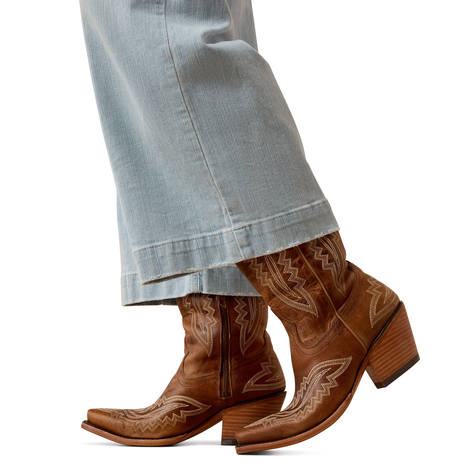 Brown cowboy boots with intricate designs worn with light blue jeans on a white background