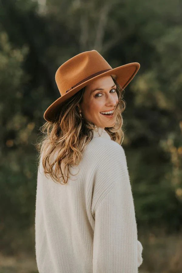 Sundaise Rhiannon Panama Hat. Woman wearing a brown hat and white sweater against a blurred natural background