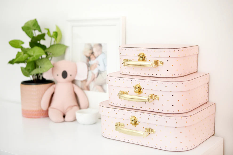 Set of pink storage boxes with gold handles on a white surface, surrounded by decorative items.