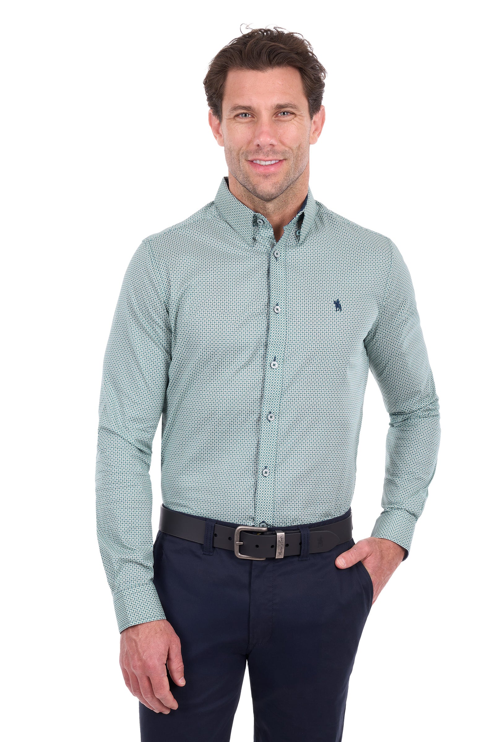 A man wearing a light sage green long-sleeve button-down shirt with a small micro-pattern, paired with dark navy trousers and a black belt, photographed against a solid white background.