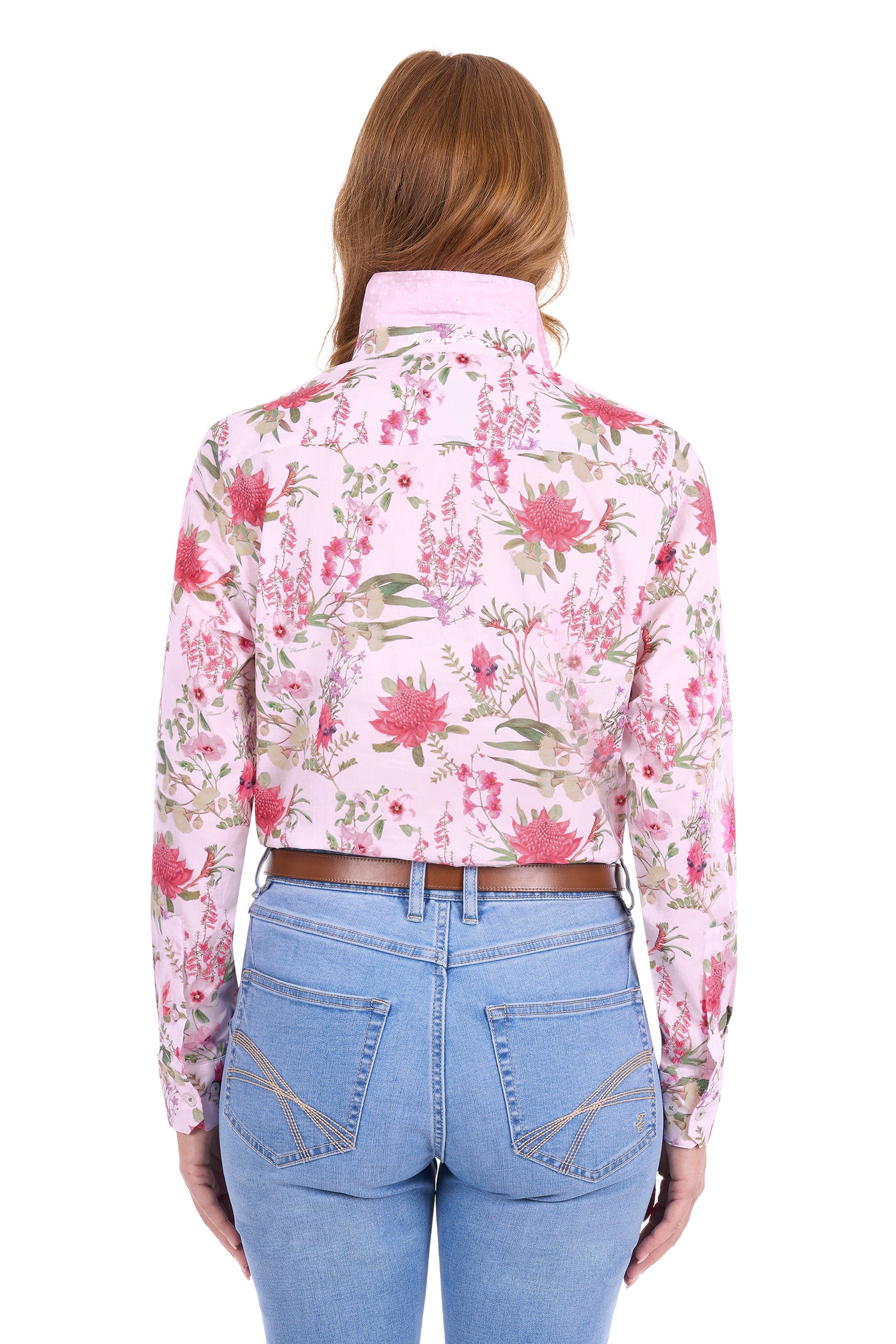 A woman viewed from the back wearing a light pink long-sleeve button-up shirt with a red and green floral print, tucked into light blue jeans.