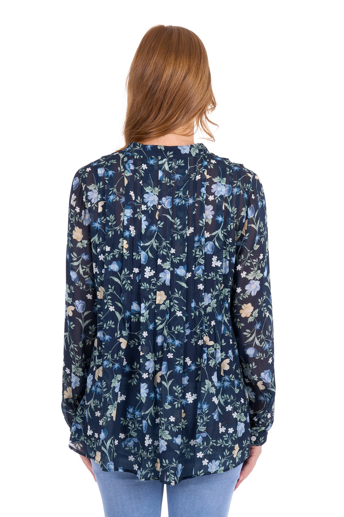 A woman viewed from the back wearing a long-sleeve navy blue blouse with a dense light blue, white, and beige floral pattern, paired with light blue jeans against a plain white background.
