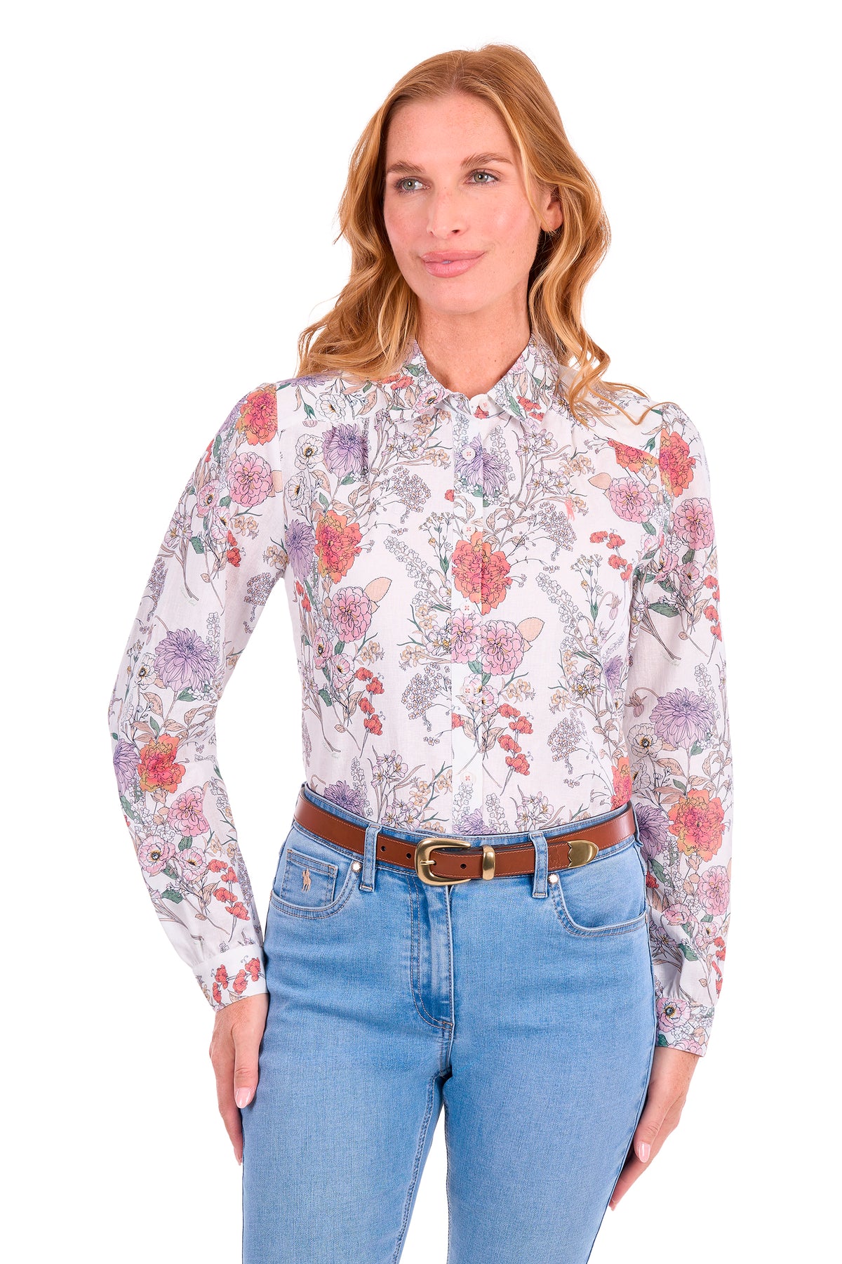 A woman modeling a long-sleeve button-up blouse with a multicolor floral and botanical print on a white base, paired with blue jeans and a brown belt, against a plain white background.