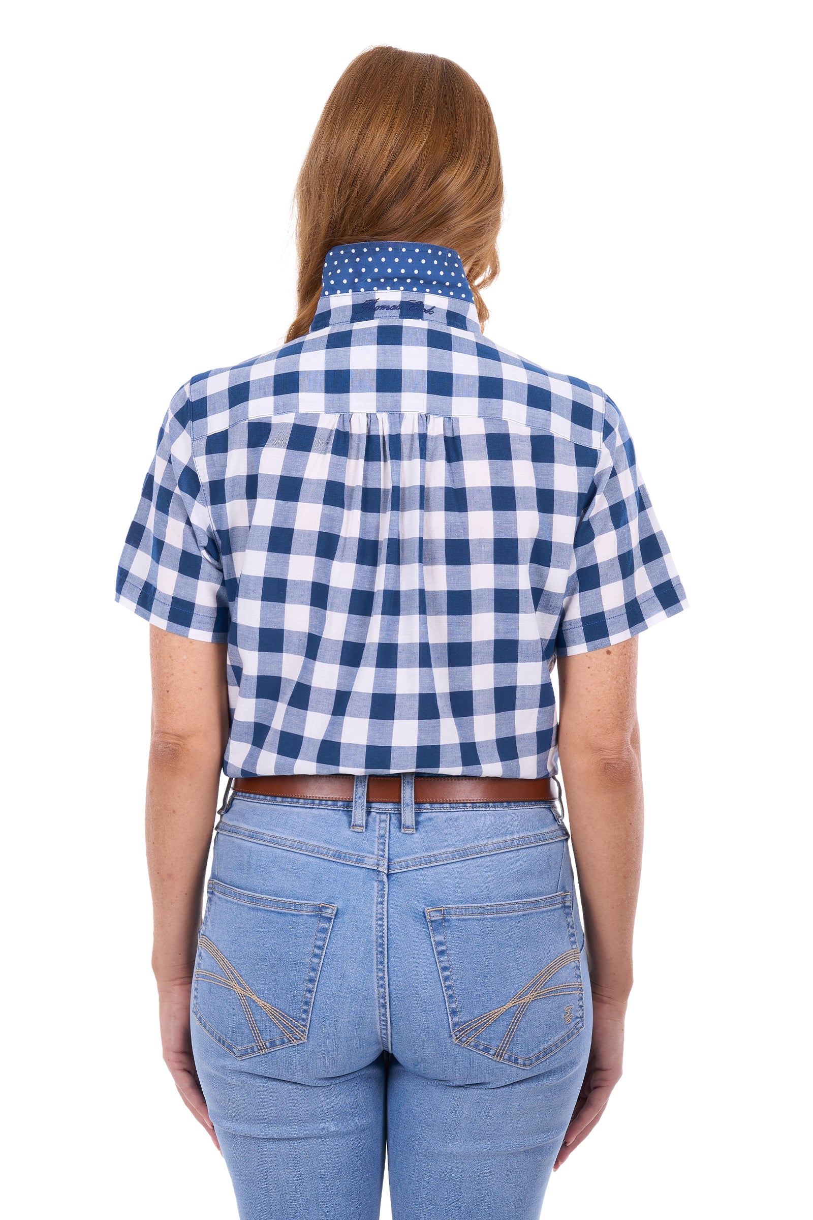 A woman viewed from the back wearing a blue and white gingham short-sleeve button-up shirt tucked into light-wash blue jeans with a brown belt.