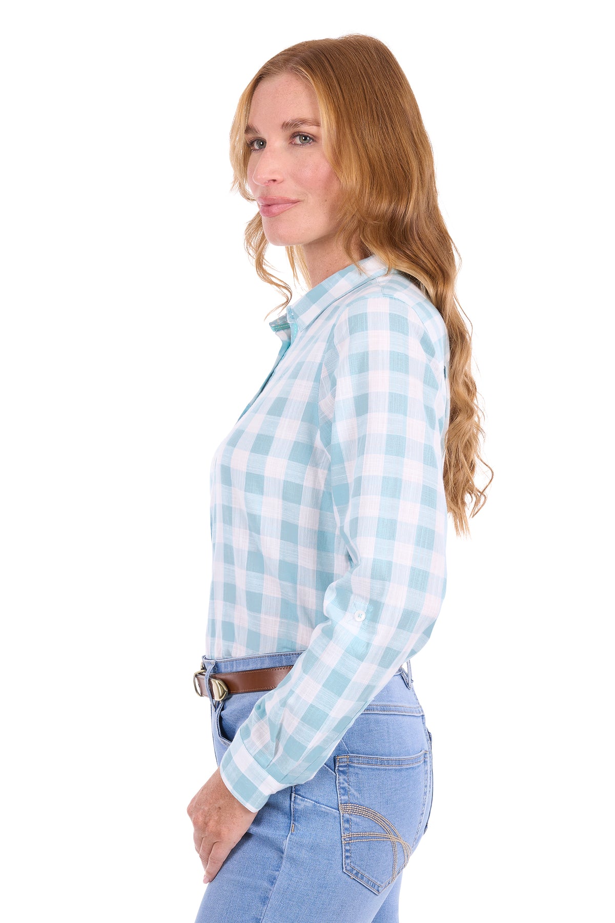 A woman with long wavy light brown hair is shown in profile wearing a light blue and white gingham long-sleeve button-down shirt, tucked into light-wash blue jeans with a brown belt, against a solid white background.