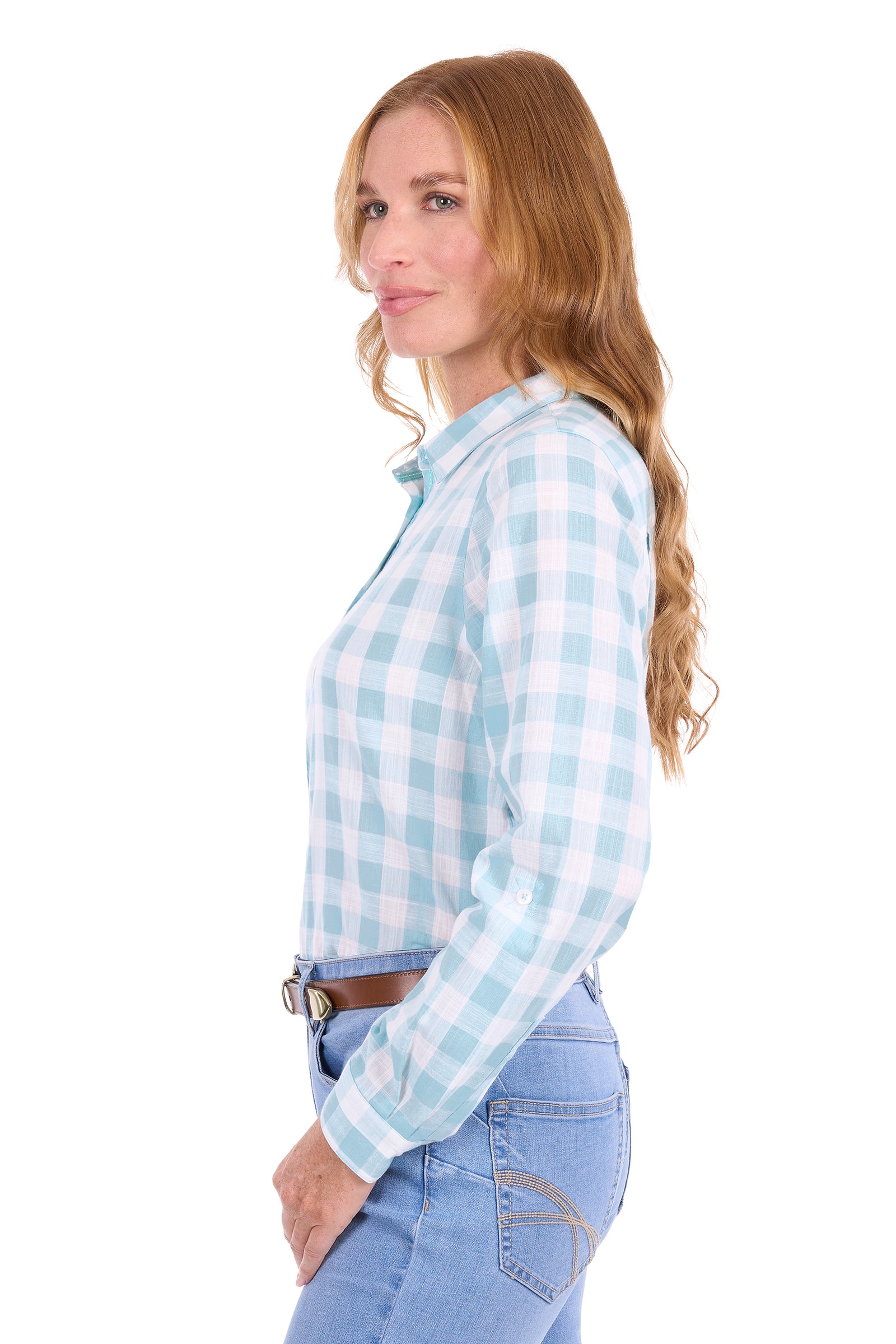 A woman with long wavy light brown hair is shown in profile wearing a light blue and white gingham long-sleeve button-down shirt, tucked into light-wash blue jeans with a brown belt, against a solid white background.