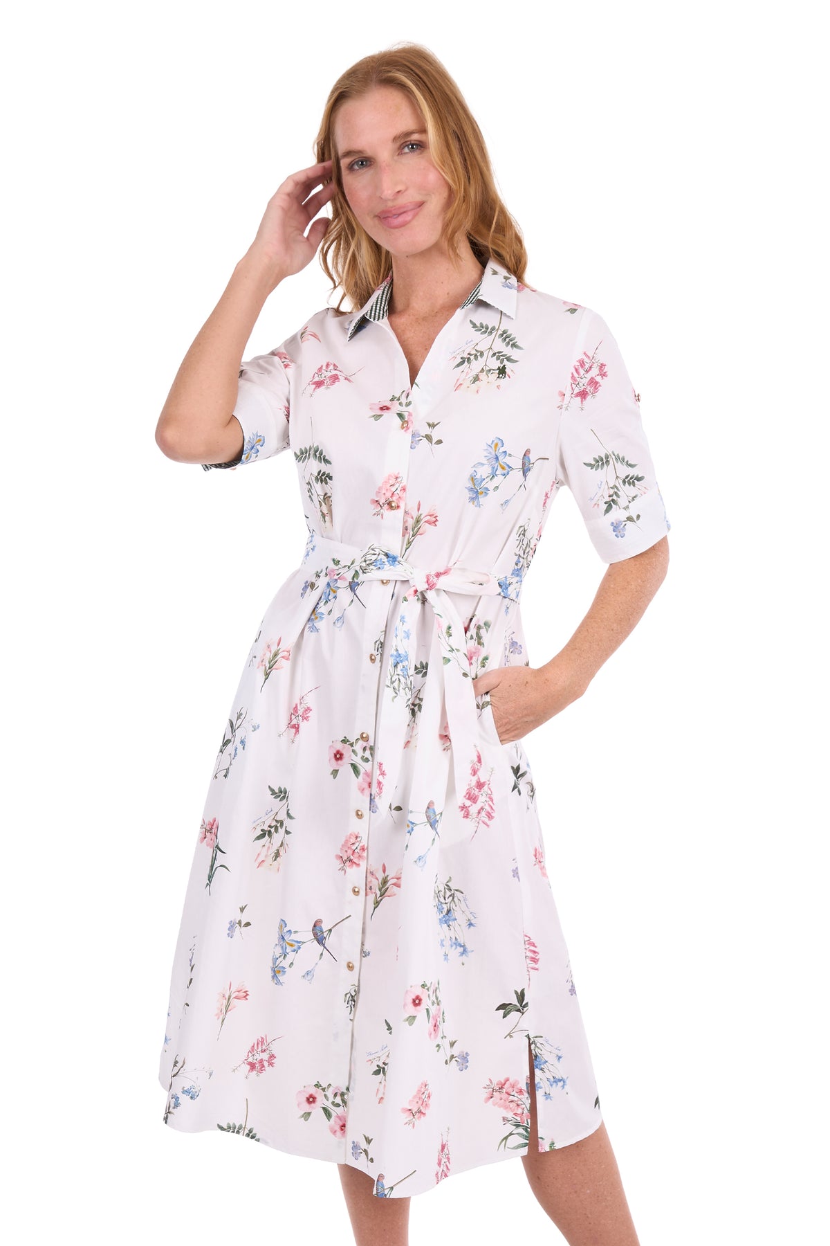 A woman modeling a short-sleeve white button-up dress with a colorful floral print and a matching tie belt, set against a plain white background.