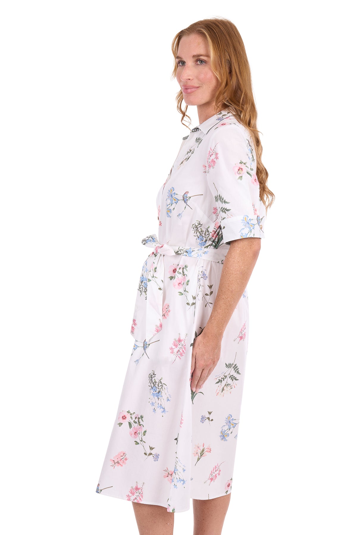 A woman modeling a short-sleeve collared dress with a matching waist tie, featuring a white base with a delicate pink, blue, and green floral print, set against a plain white background.