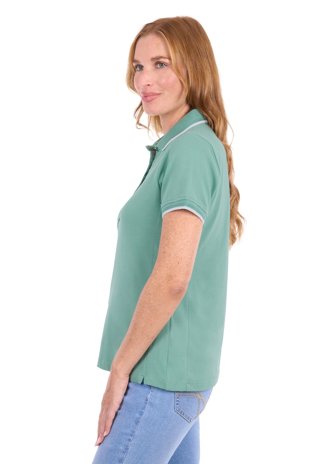 A woman shown in side profile wearing a sage green short-sleeve polo shirt with white piping on the collar and sleeve cuffs, paired with light blue jeans, against a plain white background.