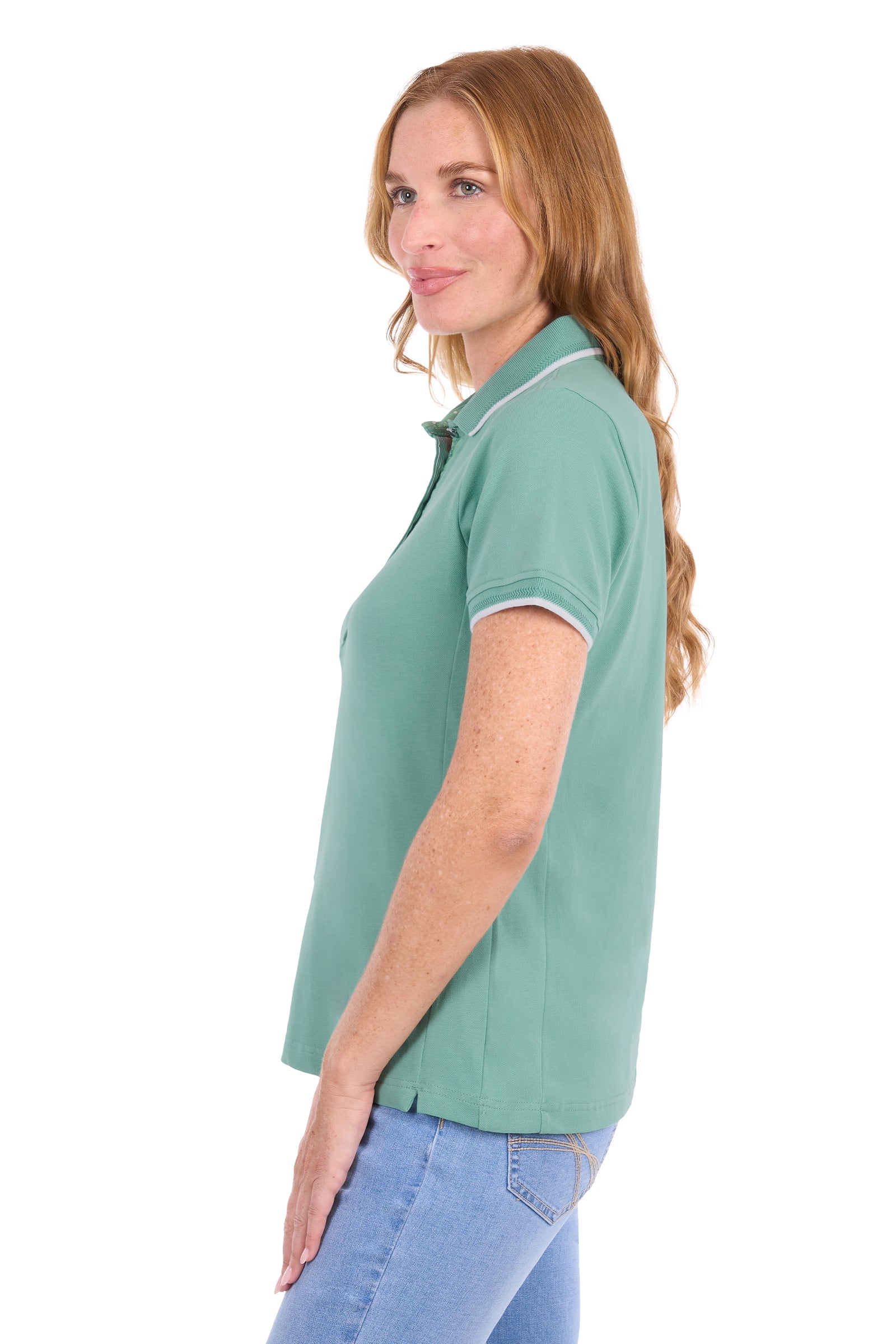A woman shown in side profile wearing a sage green short-sleeve polo shirt with white piping on the collar and sleeve cuffs, paired with light blue jeans, against a plain white background.