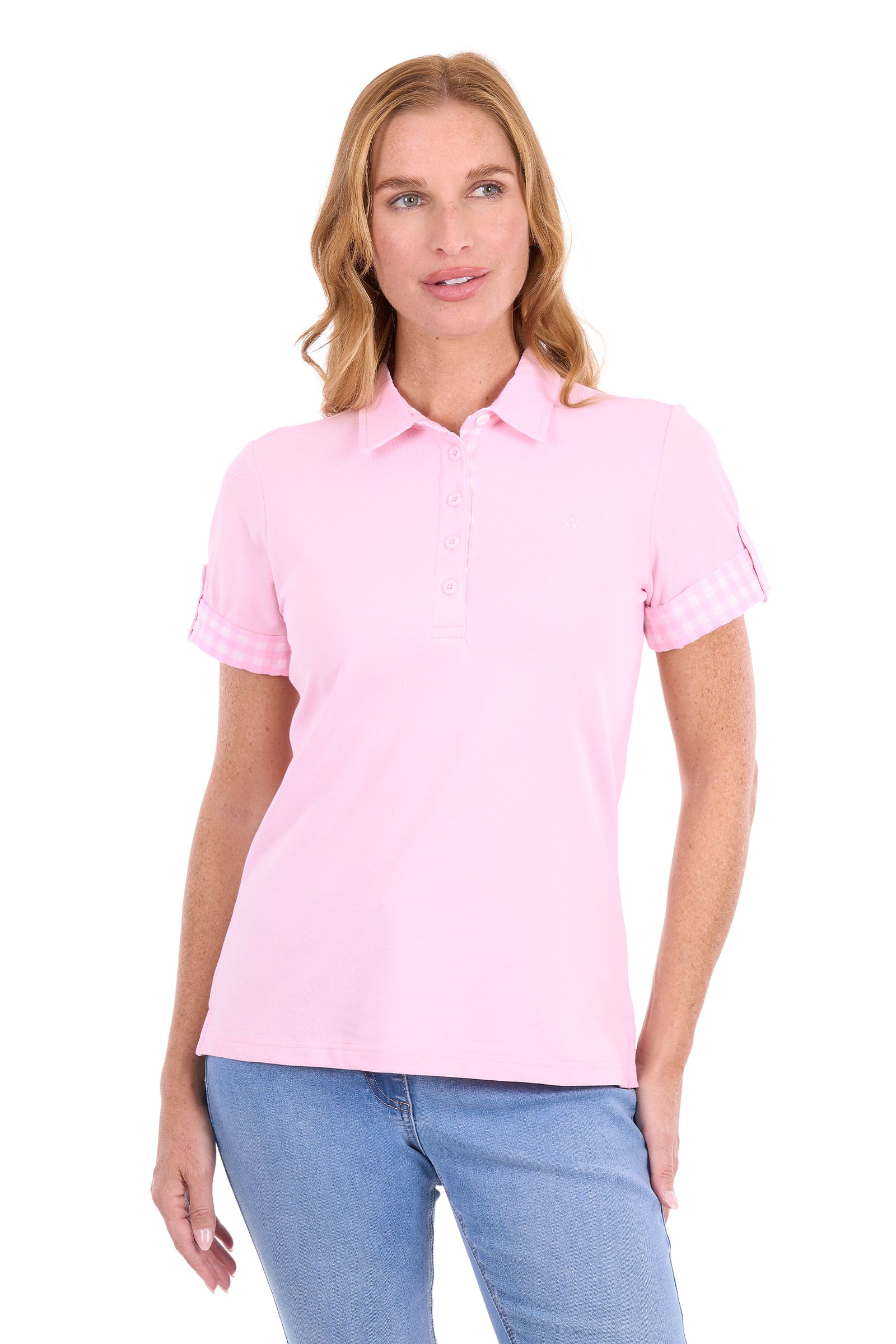 A woman modeling a light pink short-sleeve polo shirt with rolled cuffs and a button placket, paired with blue jeans, against a plain white background.