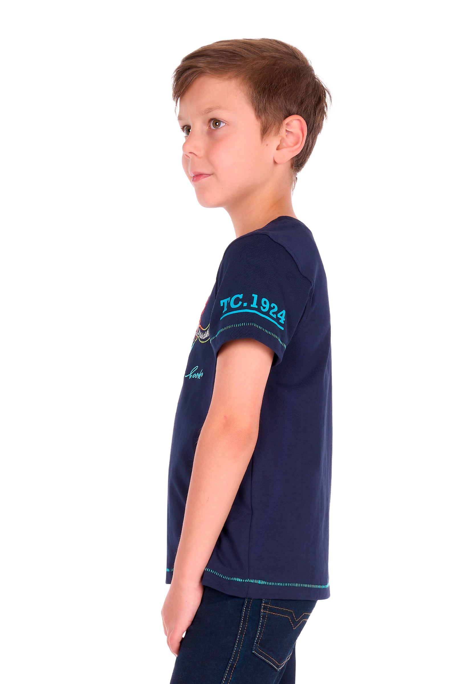 A young boy in profile wearing a navy blue short-sleeve t-shirt with teal lettering on the sleeve, paired with dark jeans, against a solid white background.
