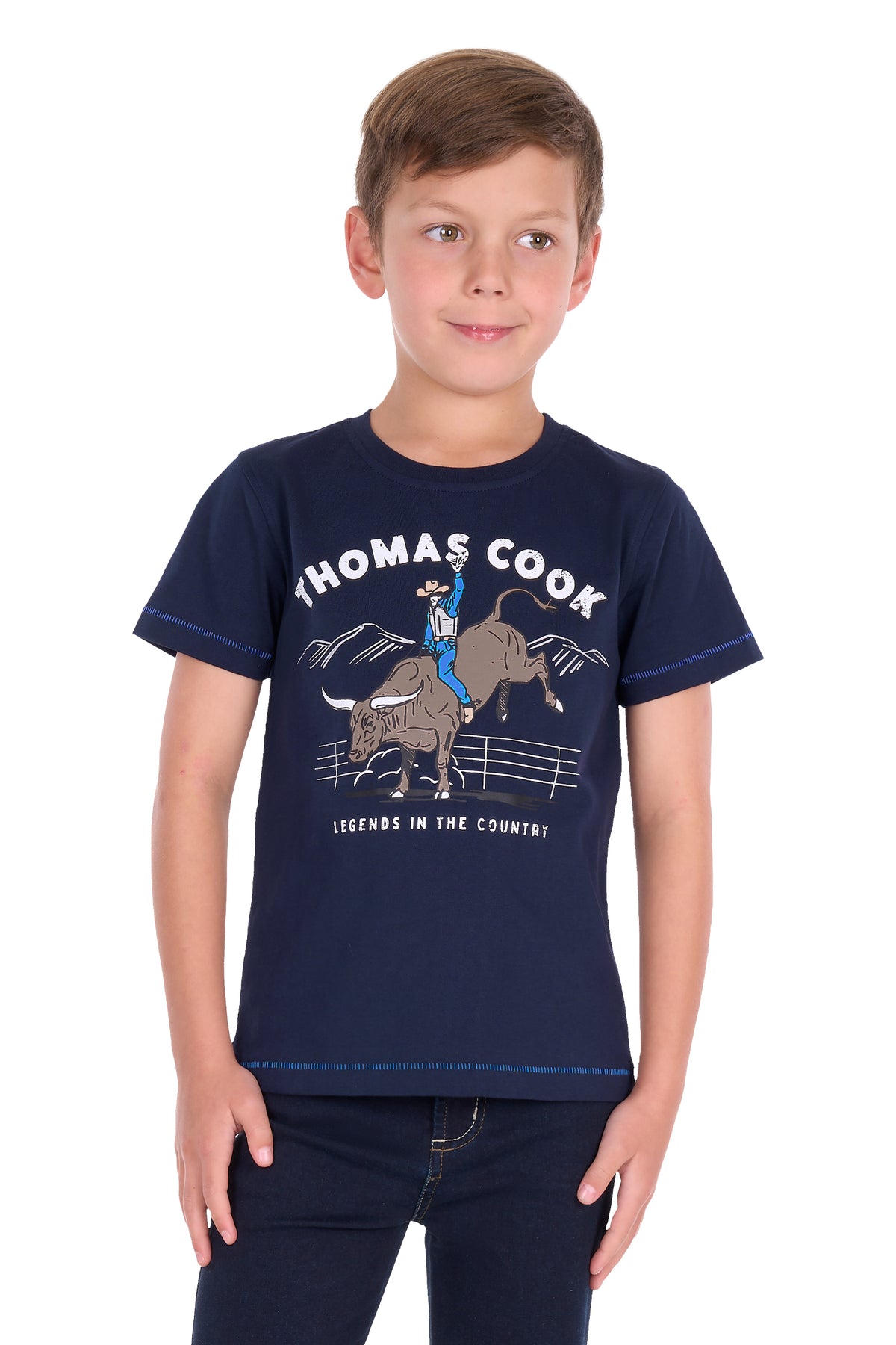 A young boy wearing a navy blue short-sleeve graphic t-shirt with 'THOMAS COOK' and a cowboy riding a bucking bull printed on the front, paired with dark jeans, against a plain white background.