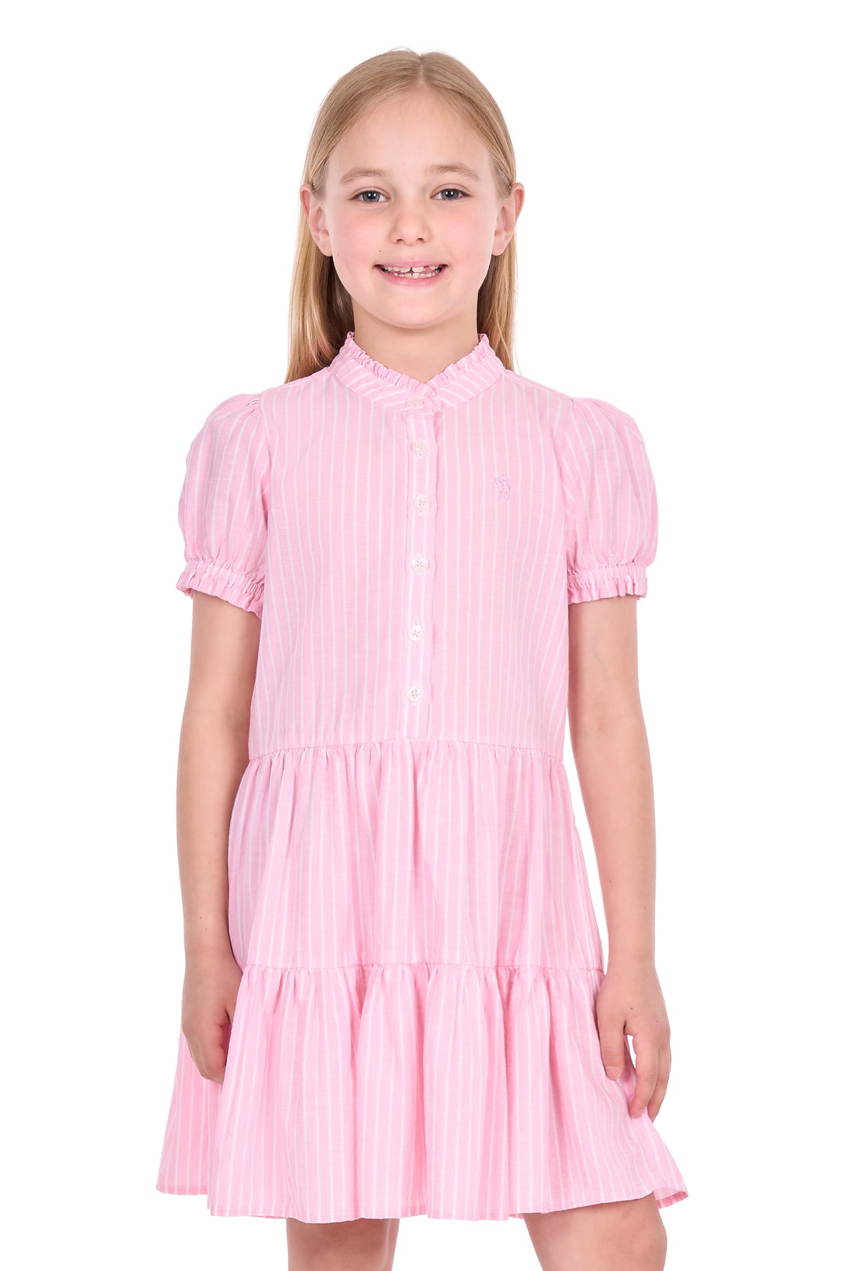 A young girl with blonde hair wearing a pink and white vertically striped tiered dress with short puff sleeves and a button-up front, standing against a plain white background.