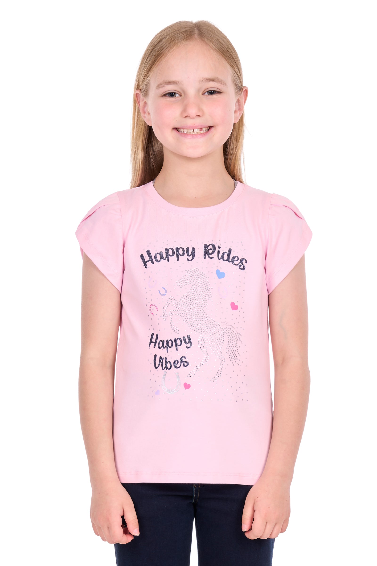 A young girl with blonde hair smiling, wearing a light pink short-sleeve t-shirt with 'Happy Rides Happy Vibes' and a unicorn graphic printed on the front, paired with dark pants, against a plain white background.