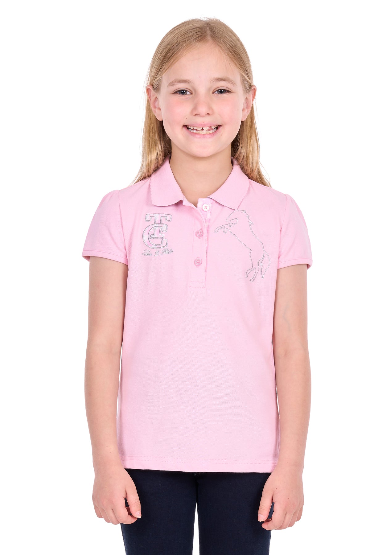 A young girl with blonde hair smiling, wearing a light pink short-sleeve polo shirt with white embroidered graphics on the chest, paired with dark pants, against a plain white background.