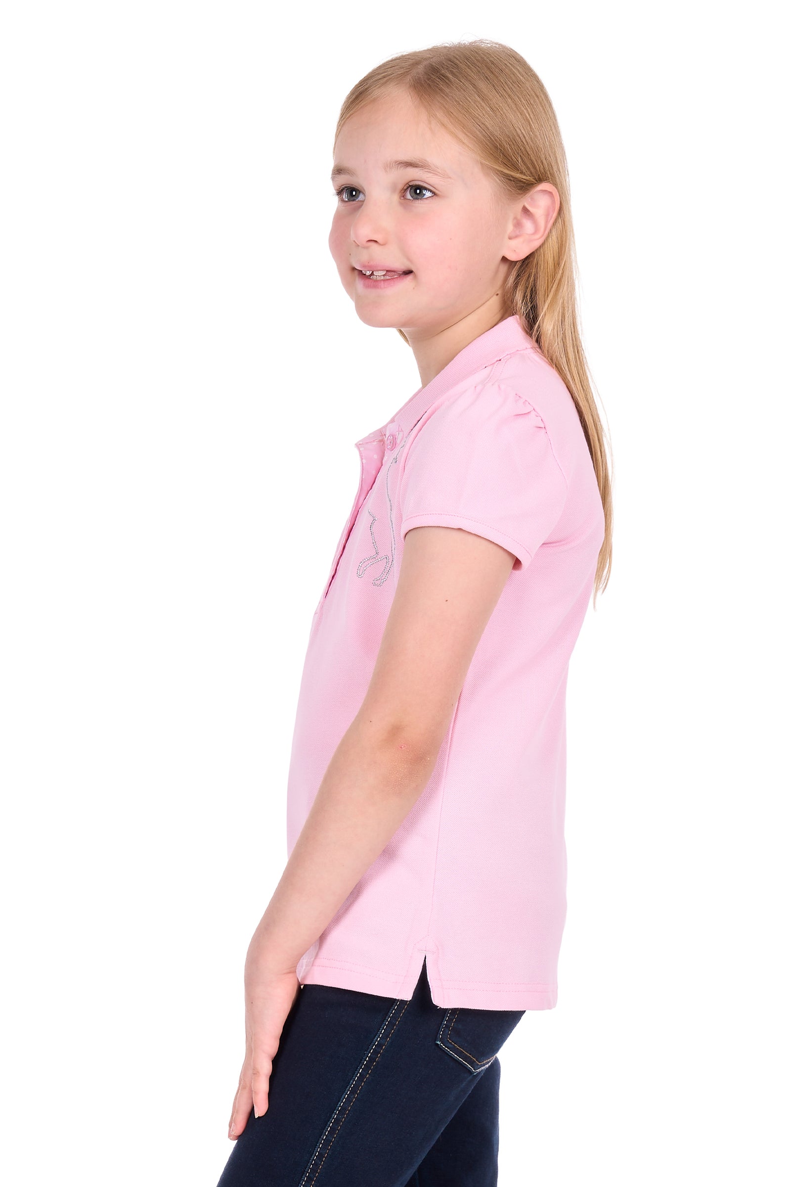 A young girl with blonde hair tied back, wearing a light pink short-sleeve polo shirt and dark jeans, shown in profile against a solid white background.