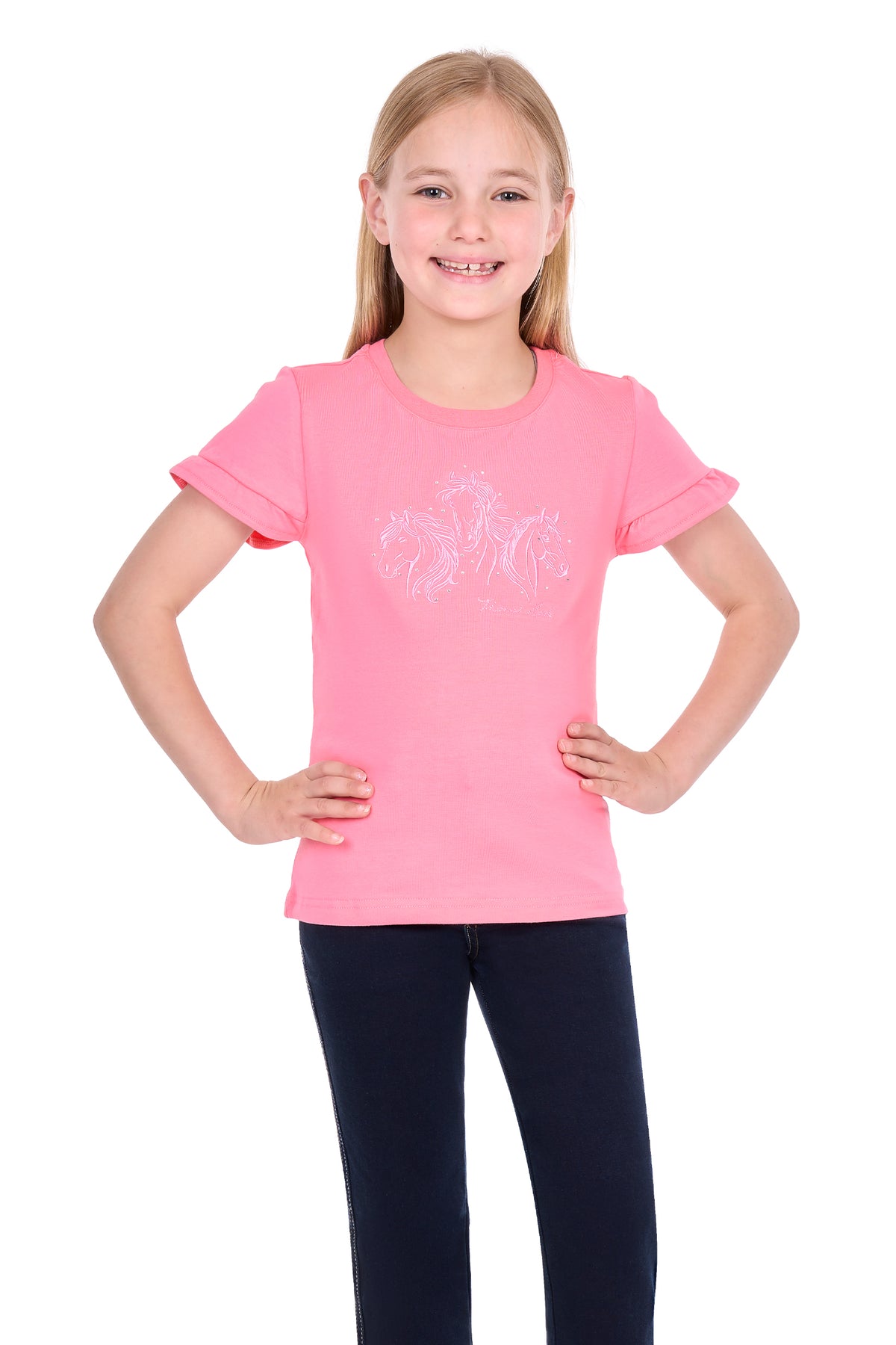 A young girl with blonde hair smiling and posing with her hands on her hips, wearing a bright pink short-sleeve t-shirt with a subtle white graphic on the front and dark navy pants, set against a plain white background.