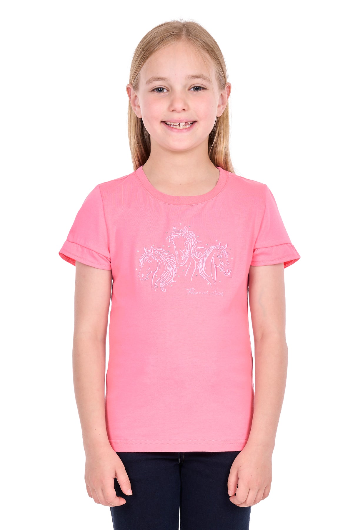 A young girl with blonde hair smiling, wearing a pink short-sleeve t-shirt with a white graphic print of three horses on the front, paired with dark pants, against a plain white background.