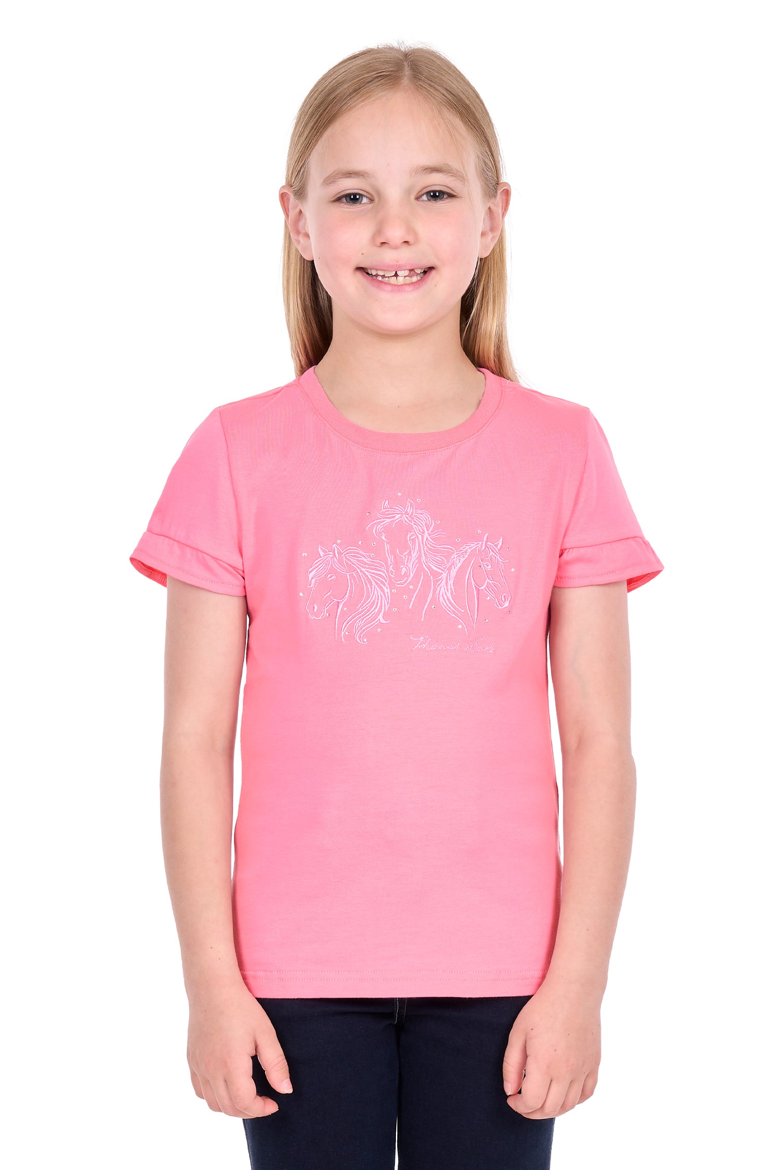 A young girl with blonde hair smiling, wearing a pink short-sleeve t-shirt with a white graphic print of three horses on the front, paired with dark pants, against a plain white background.