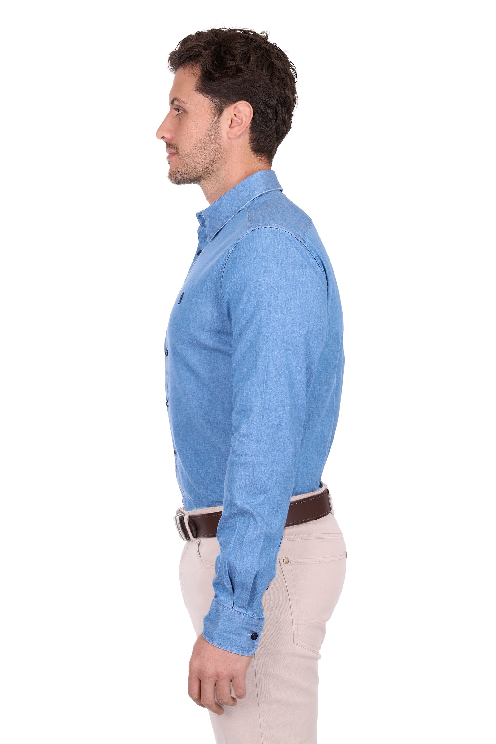 Man wearing a light blue dress shirt with a dark belt and beige pants, standing against a plain background.