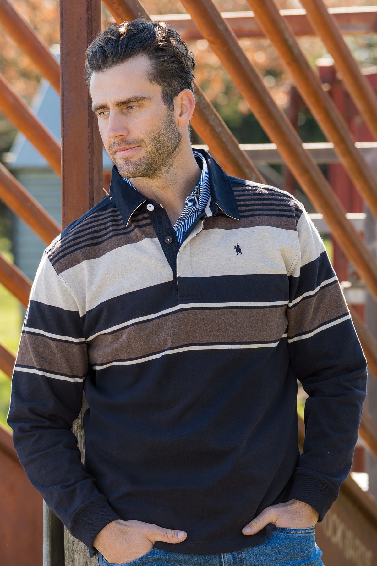 Man wearing a striped long-sleeve shirt leaning against a metal structure.