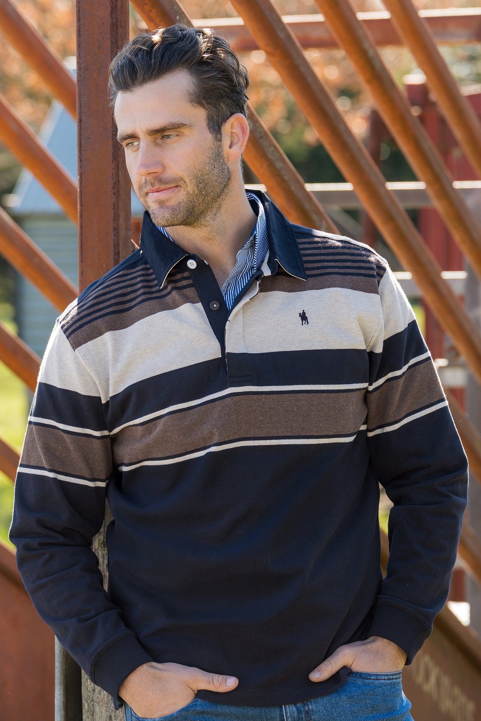 Man wearing a striped long-sleeve shirt leaning against a metal structure.
