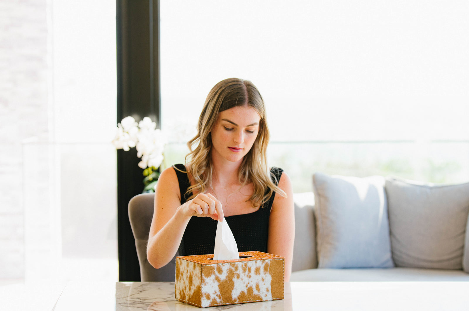 Woman sitting on a couch using a tissue from a box.