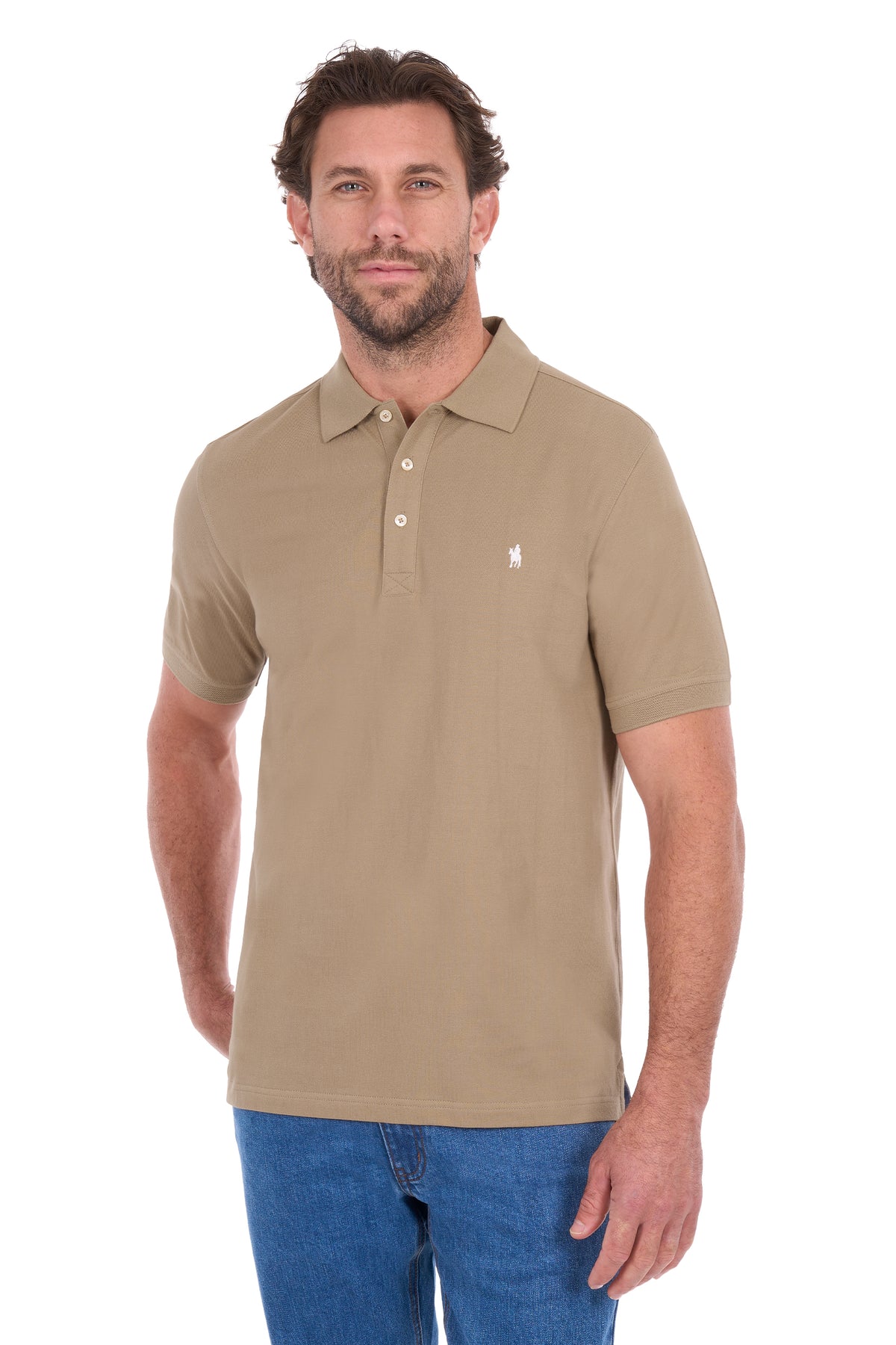 A man wearing a tan short-sleeve polo shirt with a small white embroidered logo on the left chest, paired with blue jeans, against a plain white background.