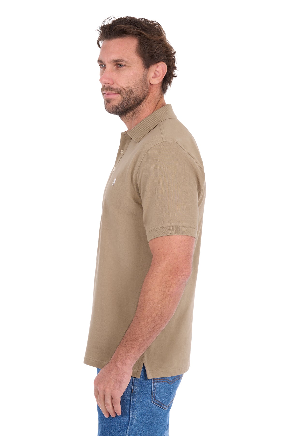 A man shown in profile wearing a short-sleeve polo shirt in a warm khaki-beige color, paired with blue jeans, against a plain white background.