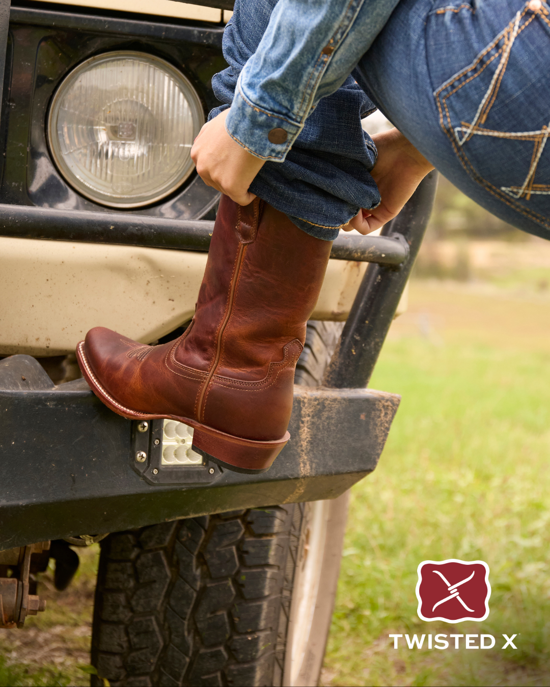 Person wearing brown cowboy boots and blue jeans standing on a vehicle with 'Twisted X' logo.