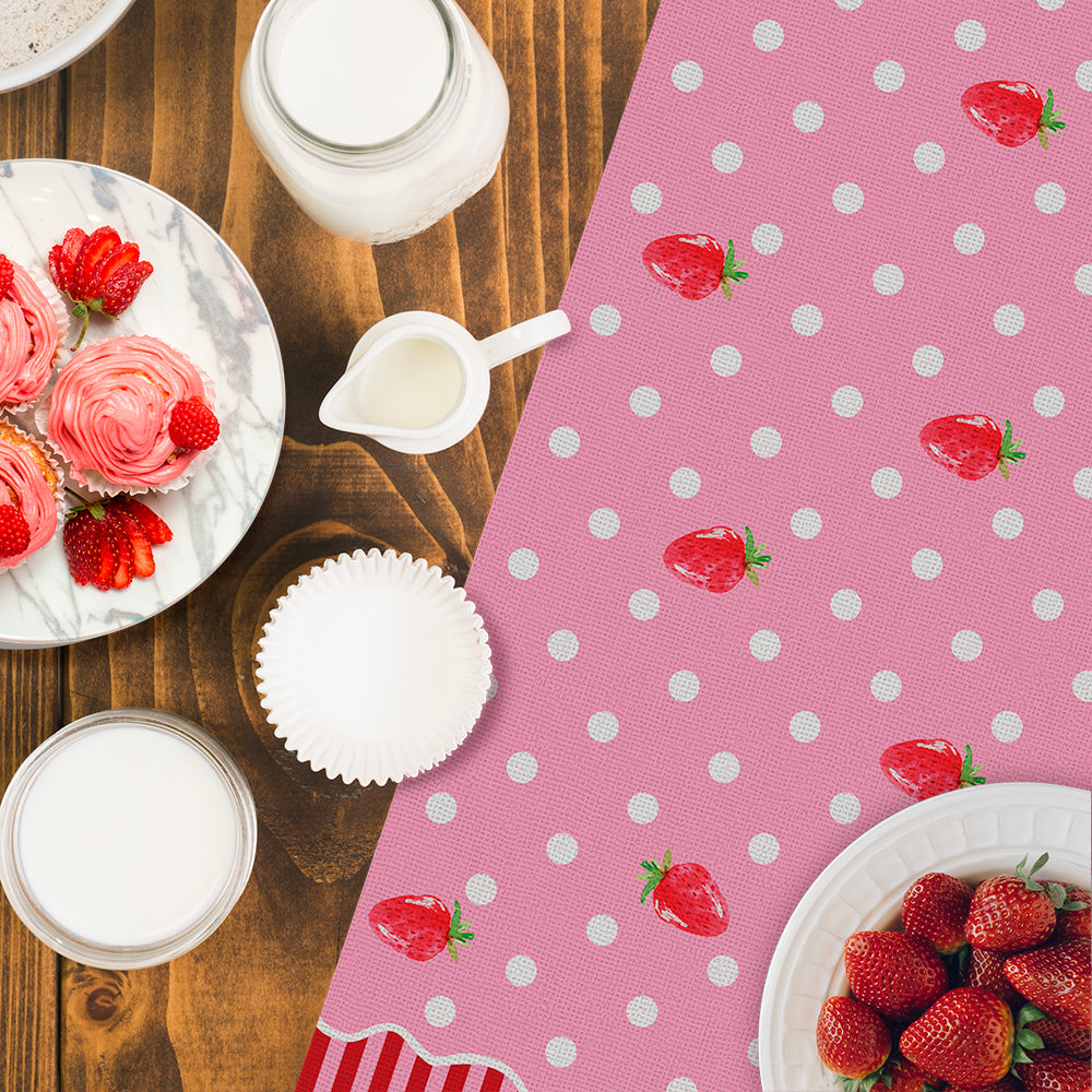 Table setting with pink polka dot tablecloth, strawberries, and pink cupcakes on a wooden surface.