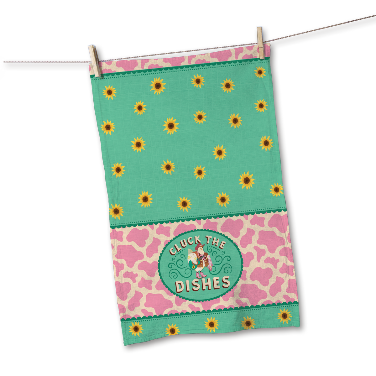 A decorative kitchen towel hanging from a clothesline with a wooden clothespin. The towel features a mint green top section with yellow sunflower patterns, a pink and beige cow-print middle band, and a central green oval patch that reads 'CLUCK THE DISHES' with a cartoon cow.