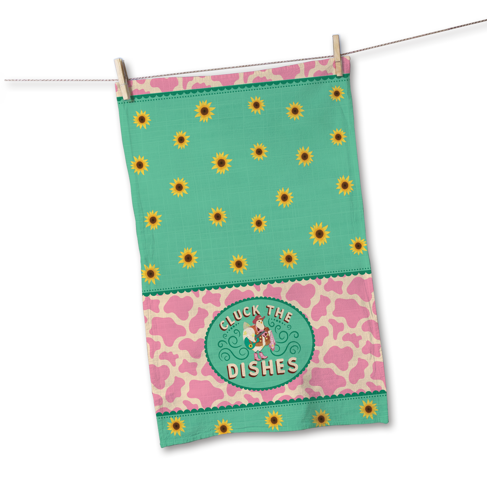 A decorative kitchen towel hanging from a clothesline with a wooden clothespin. The towel features a mint green top section with yellow sunflower patterns, a pink and beige cow-print middle band, and a central green oval patch that reads 'CLUCK THE DISHES' with a cartoon cow.