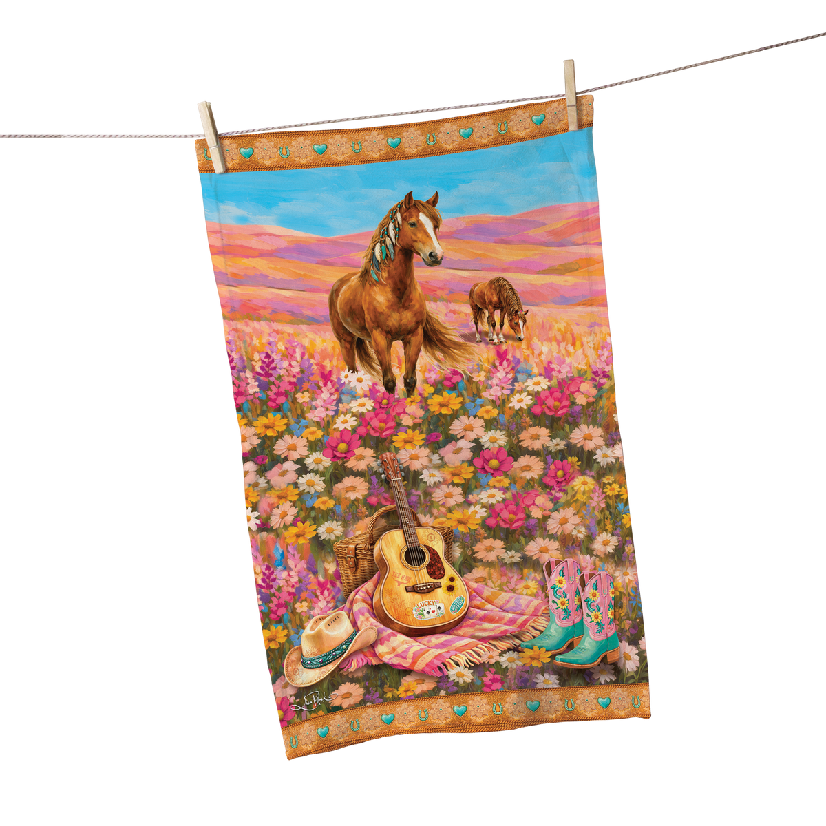 A rectangular printed towel or cloth hanging from a clothesline with two wooden clips. The fabric features a colorful western-style illustration of horses in a flower field, with a guitar, hat, boots, and a striped blanket near the bottom.
